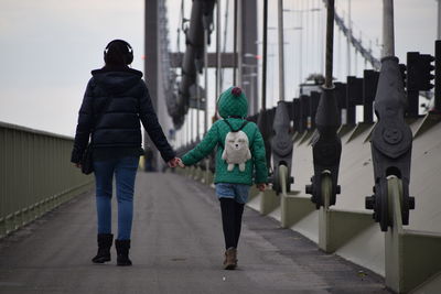 Rear view of mother and daughter holding hands while walking on bridge