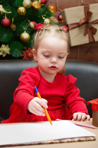 A little girl in a red dress draws on the background  a decorated christmas tree and presents writes