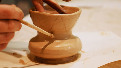 Cropped hands of craftsperson making clay product in pottery workshop