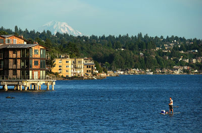 Man paddleboarding on lake with buildings in background