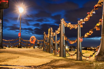 Illuminated street lights by road against sky at night