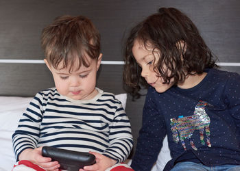 Brother and sister playing a video game on a hotel bed