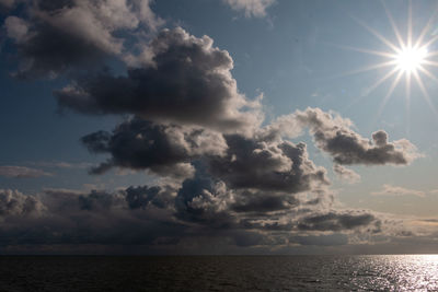 Low angle view of sunlight streaming through clouds over sea