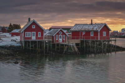 House by river against sky during sunset