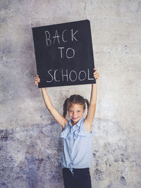 Portrait of smiling girl holding writing slate with text against wall