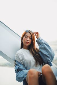 Portrait of beautiful young woman sitting against sky