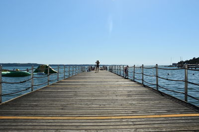 Rear view of man standing on pier at sea against clear sky