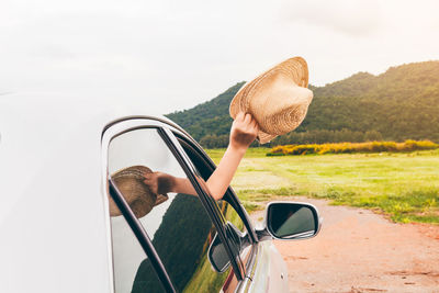 Woman holding straw hat outside car window