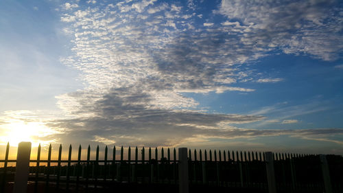 Silhouette fence by building against sky during sunset