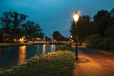 Illuminated street by river against sky at night