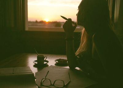 Woman holding umbrella while standing by window