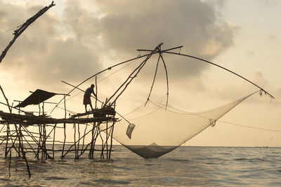 Silhouette man fishing in sea against sky during sunset