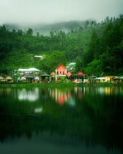 Houses by lake and buildings against sky