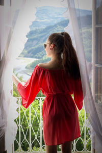 Young woman looking through window at home