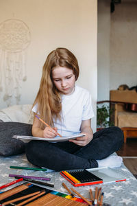 The girl after school plays at home, draws with pencils and felt-tip pens