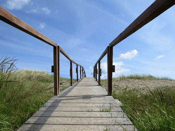 Empty boardwalk against cloudy sky