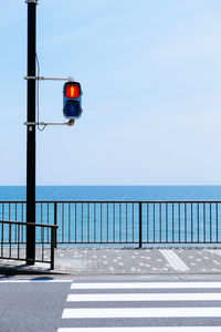 Road signal on street by sea against clear sky