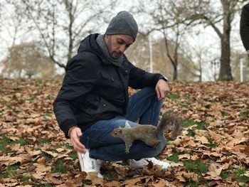 Portrait of man sitting on field with squirrel