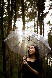 Portrait of young woman with umbrella standing in forest