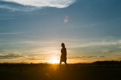 Silhouette teenage girl walking on land against sky during sunset