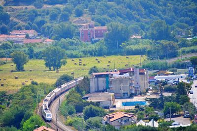 High angle view of trees, railroad with train and buildings in city