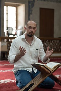 Portrait of man praying by koran at mosque