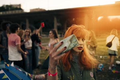 Redhead young woman taking selfie on smart phone with friends in background