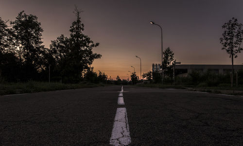 Road by trees against sky during sunset in city