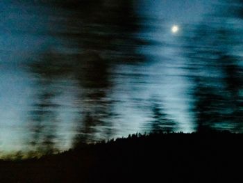 Defocused image of silhouette trees against sky at night