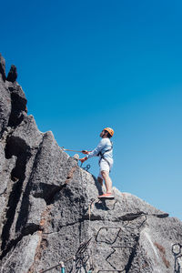 Low angle view of man on rock against clear blue sky