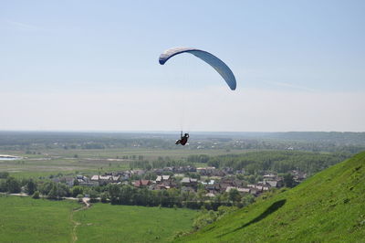 Woman paragliding over landscape against sky