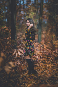 Young woman looking away while standing on tree in forest