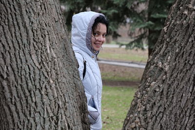 Portrait of smiling woman standing by tree trunk