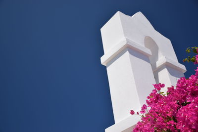 Low angle view of bougainvillea blooming by tower against clear blue sky