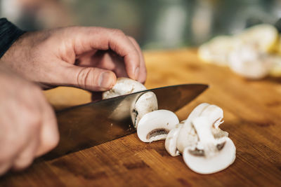 Cooking dinner - chef holding a knife, cutting mushrooms on a wooden cutting board