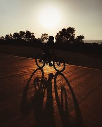 Silhouette man riding bicycle on street against sky during sunset