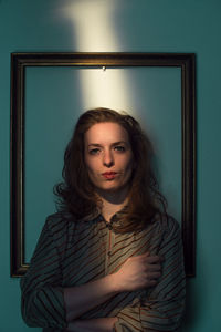 Portrait of young woman standing against wall at home