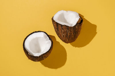 Two halves of coconut on a bright yellow background.