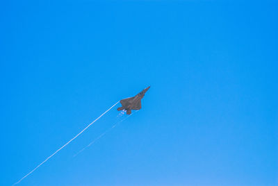 Low angle view of f22 flying against clear blue sky