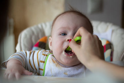 Cropped hand of woman feeding food to baby boy at home