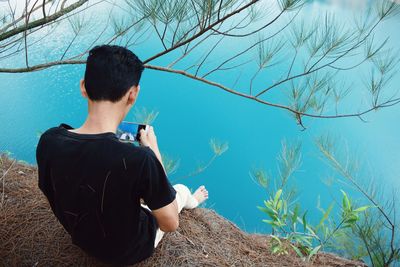 High angle view of man using mobile phone while sitting on cliff