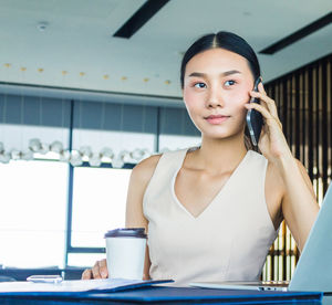 Portrait of young woman using smart phone on table