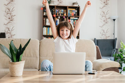 Girl schoolgirl at home in front of a laptop rejoices at success. online learning, distance 