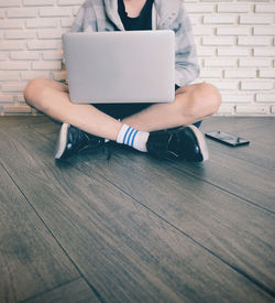 Midsection of woman using mobile phone while sitting on wooden floor