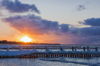 Frozen wooden posts in sea against sky