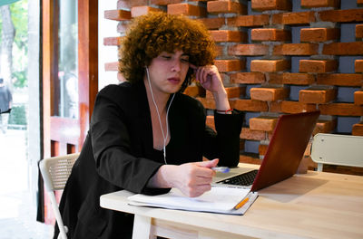 Non-binary person stops to tinking what is going to write in the notebook