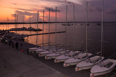 Boats moored in harbor at sunset