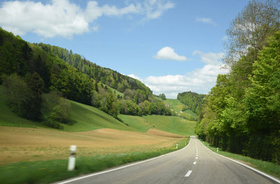 Empty road along trees and landscape against sky