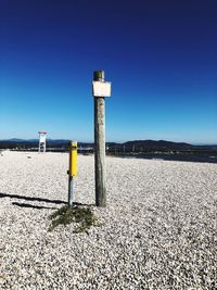 Wooden post on beach against clear blue sky