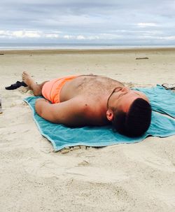 Shirtless man lying on sand at beach against sky